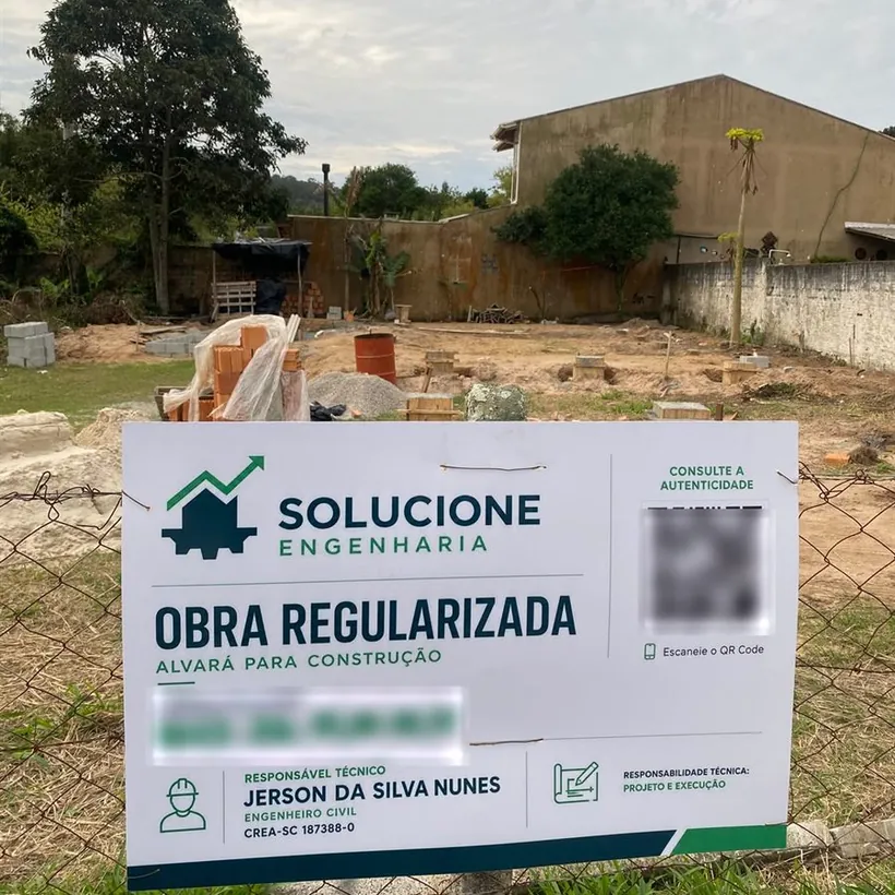 Placa da Solucione Engenharia em terreno de obra, indicando obra regularizada com alvará para construção e o responsável técnico Jerson da Silva Nunes, CREA-SC 187388-0.