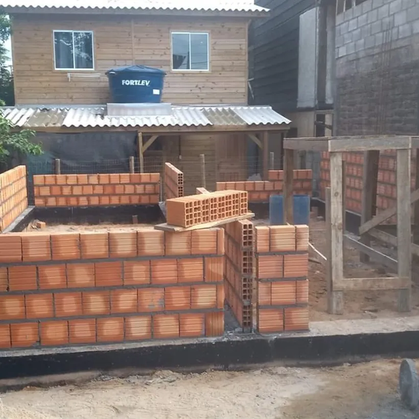 Alvenaria de blocos cerâmicos em execução sobre baldrame, com betoneira ao lado, em obra residencial.